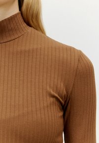 Bruine geribbelde coltrui met een aansluitend ontwerp en een zachte textuur, met verticale lijnen en een hoge kraag.