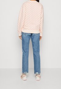 Světle růžová mikina s malými červenými tečkami, spárovaná s modrými džíny rovného střihu. Bílo-bezové tenisky dotvářejí celý outfit.