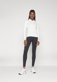 Hosszú ujjú fehér póló, sötét leggings és fehér sportcipő. Jellemzői közé tartozik a gallér és a testhezálló fazon, sima textúrával.