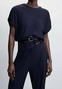 Haut texturé bleu marine à manches courtes, rentré dans un pantalon assorti, avec une ceinture noire à boucle métallique pour un détail supplémentaire.