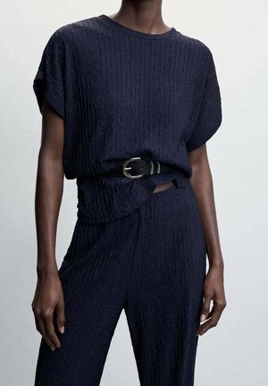 Haut texturé bleu marine à manches courtes, rentré dans un pantalon assorti, avec une ceinture noire à boucle métallique pour un détail supplémentaire.