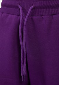 Lila Jogginghosen mit einem gerippten Bund, ausgestattet mit Kordeln und einer glatten, weichen Baumwolltextur. Nahaufnahme des Taillenbereichs.