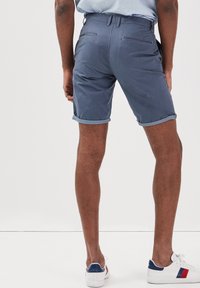 Mörkblå, knälånga shorts med en texturerad tyg; upprullad nederkant; två bakfickor; bärs med vita sneakers med blå och röda accenter.