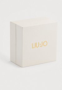 Balts teksturēts taisnstūra kaste ar zelta "LIU JO" logotipu, centrēts uz sāna, uzņemts uz vienkārša balta fona.