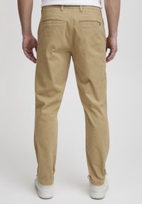 Pantalon en coton beige à coupe droite, doté de deux poches arrière et d'une texture lisse. Porté avec des baskets blanches.