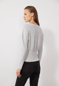 Grijze geribbelde lange mouw top met een aansluitende taille, gecombineerd met zwarte jeans. De stof heeft een zachte textuur en een natuurlijke rek.