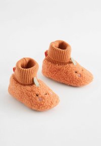 Orange, fluffiga babystövlar med en ribbad stickad krage, prydda med broderade ansiktsdetaljer och en liten grön bladaccent.