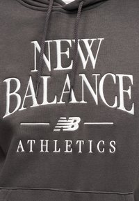 Σκούρα γκρι φούτερ με κουκούλα με λευκό κεντημένο κείμενο "NEW BALANCE ATHLETICS" και το λογότυπο της New Balance ανάμεσα στις λέξεις.
