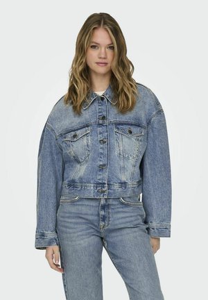 Giacca di jeans blu tagliata con maniche lunghe, due tasche sul petto, chiusura con bottoni e dettagli di leggero sbiadimento, abbinata a jeans coordinati.