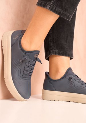 Blue sneaker with a textured surface, round toe, and flat cream-colored sole. Features subtle logo and traditional lace-up design.