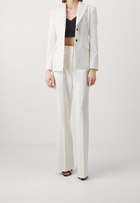Biały, dopasowany żakiet zapinany na jeden guzik, w zestawie z pasującymi szerokimi spodniami i czarnym, krótkim topem. Czarne sandały na wysokim obcasie.