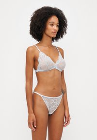 Lingerie set pitsit, ikilisi ibhande eliluhlaza okwesibhakabhaka, i-triangle bralette enezintambo ezilungiswayo, kanye ne-thong ehlanzekile ehambisanayo. Iphattern ebhalwe ngezimbali.