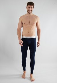 Leggings de color navy hechos de tela elástica, con una cintura elástica en gris claro que lleva el logo de "TOM TAILOR". Se ajustan al cuerpo de forma ceñida.
