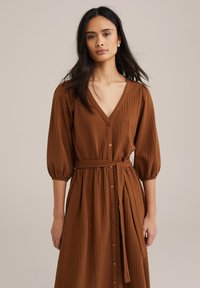 Brun knappupp klänning med V-ringning, 3/4 puffärmar, midja med bälte och texturerad tyg. Har en helängdsdesign med en avslappnad passform.