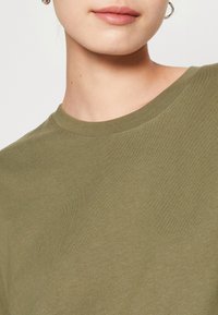 Oliwkowa, krótko rękawowa koszulka z miękkiej bawełny, z okrągłym dekoltem i gładką teksturą z delikatnym streczem.