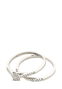 Juego de dos anillos de plata, uno con un grupo de pequeñas piedras brillantes transparentes y el otro con una banda lisa. Ambos presentan un diseño minimalista.