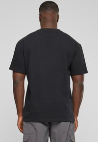 T-shirt en coton noir avec une coupe décontractée, des manches courtes et un col rond. Design sobre sans motifs ni logos.