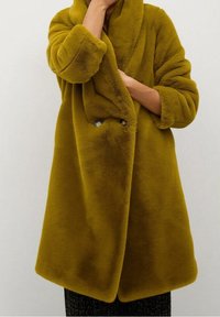 Manteau jaune moutarde pelucheux avec un large col, des manches longues et une fermeture à double bouton. Texture douce avec une coupe décontractée.