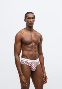 Biała gumka w pasie z logo „Calvin Klein”, czerwony geometryczny wzór na rozciągliwych majtkach, o dopasowanym kroju i gładkiej fakturze.