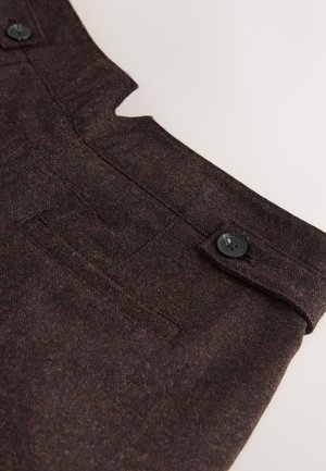 Donkerbruin stof met een subtiele textuur. Voorzien van een uitsnijdingsontwerp, een zak en een zwart knoopaccent.