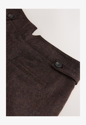Donkerbruin stof met een subtiele textuur. Voorzien van een uitsnijdingsontwerp, een zak en een zwart knoopaccent.