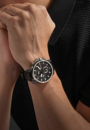 Schwarze Chronographuhr mit silbernen Akzenten, strukturiertem schwarzen Lederarmband und mehreren Zifferblättern. Metallgehäuse mit polierter Oberfläche.