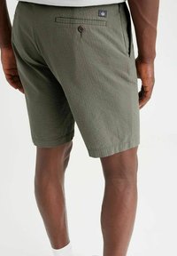 Pantaloni corti verdi realizzati in tessuto testurizzato, con una vestibilità rilassata, che presentano tasche laterali e una tasca posteriore con chiusura a bottone.