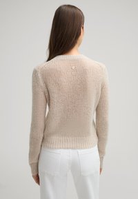 Heller beiger, gestrickter Pullover mit lässiger Passform, geripptem Saum und einem kleinen Logo-Detail am Nacken. Weiches, strukturiertes Garn.