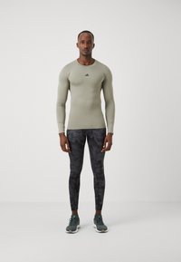 Light green long-sleeve athletic top with black logo, paired with fitted black leggings featuring a textured pattern and dark gray sneakers.