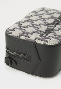 Compact rechthoekige tas met een grijze geweven stof met een herringbone patroon en zwarte leren accenten. Zijritssluiting en logo-detail.