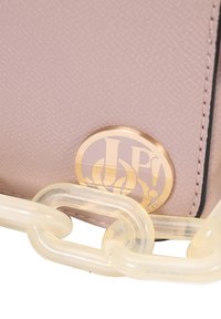 Sac à main texturé rose avec un logo circulaire doré et une bandoulière en chaîne translucide. Le design comprend des coutures noires contrastées.