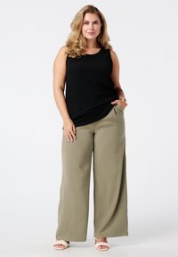Zwarte geribde tanktop in combinatie met wijde olijfgroene broek. De outfit heeft een ontspannen pasvorm en lichte stof. De schoeisel is lichtroze sandalen.