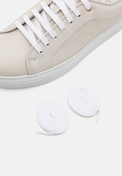 Light beige leather sneaker with white laces and rubber sole. Two additional white shoelaces are displayed next to the shoe.