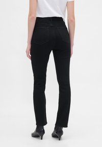 Črne kavbojke z visokim pasom, ozko krojene, s petimi žepi in subtilnim zadnjim ojačanjem, kombinirane s črnimi čevlji z visokimi petami.