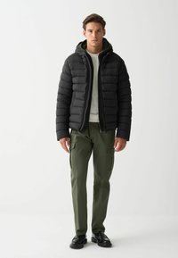 Melna pūkaina jaka ar kapuci, ar kvadrātveida šuvēm. Valkāta virs gaiša džempera un kombinēta ar olīvzaļām kargo biksēm un melniem apaviem.