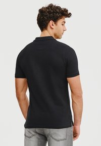 Czarna koszulka polo z krótkim rękawem, wykonana z bawełny, z klasycznym kołnierzykiem i bocznymi rozporkami dla wygody. Noszona z jasnoszarymi dżinsami.