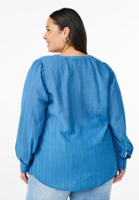 Blaue Bluse mit langen Ärmeln, vertikalen Streifen, rundem Ausschnitt und gepufften Ärmeln. Weicher, strukturierter Stoff mit geknöpften Manschetten.