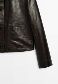 Veste en cuir marron foncé avec boutons noirs et une grande poche avant carrée, montrée de la taille vers le bas et une manche sur fond blanc.