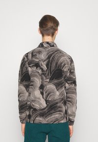 Langarmshirt met een zwart en grijs draaiend patroon, voorzien van een zachte textuur en een kraag, gedragen met blauw-groene broek.