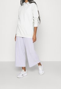 Sudadera gris claro con cordón, pantalones anchos lavanda con un acabado texturizado y zapatillas blancas. Diseño simple y de ajuste relajado.