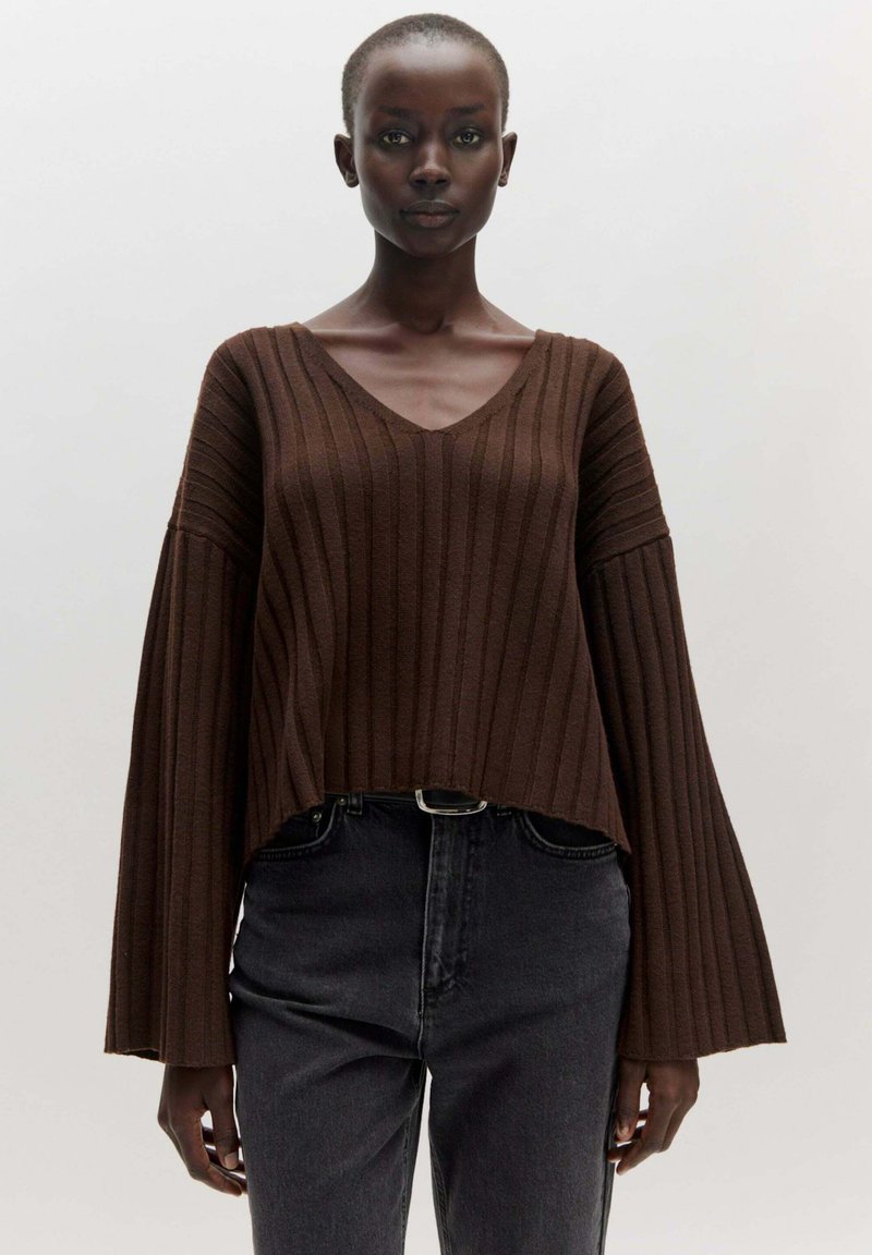 Brown ribbed knit sweater with a v-neckline and flared sleeves, paired with high-waisted black jeans. Smooth texture, casual design.