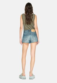 Top a righe verde, pantaloncini di jeans azzurri con orlo sfrangiato e sandali spessi azzurri chiari con marchio nero sulla suola.