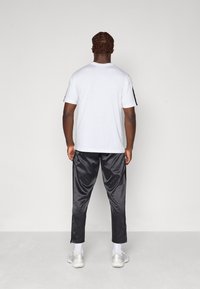 Hvid bomulds-T-shirt med korte ærmer, parret med sorte satin sweatpants. Grå sneakers med hvide detaljer og synlige ankelstrømper.