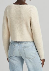 Krémový pletený svetr s texturovaným povrchem, krátké délky a širokými rukávy, spojený se světle modrými džíny s vysokým pasem.