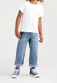 T-shirt bianco a maniche corte, jeans blu con risvolto, e sneakers alte navy con lacci bianchi. Abbigliamento casual e dalla vestibilità morbida.