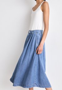 Jupe en jean bleu clair, design en A avec plis, longueur mi-mollet, dotée d'une fermeture à boutons et d'une texture lisse et propre.