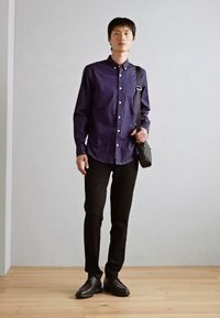 Cămașă închisă la culoare, cu nasturi, cu un model geometric subtil, asortată cu pantaloni negri slim-fit și pantofi negri eleganți; geantă crossbody inclusă.