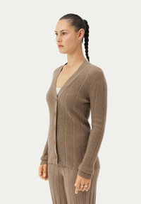 Beige ribbad kavaj med djup V-hals, knappstängning och långa ärmar; i kombination med matchande ribbad kjol. Mjuk textur och figurnära design.