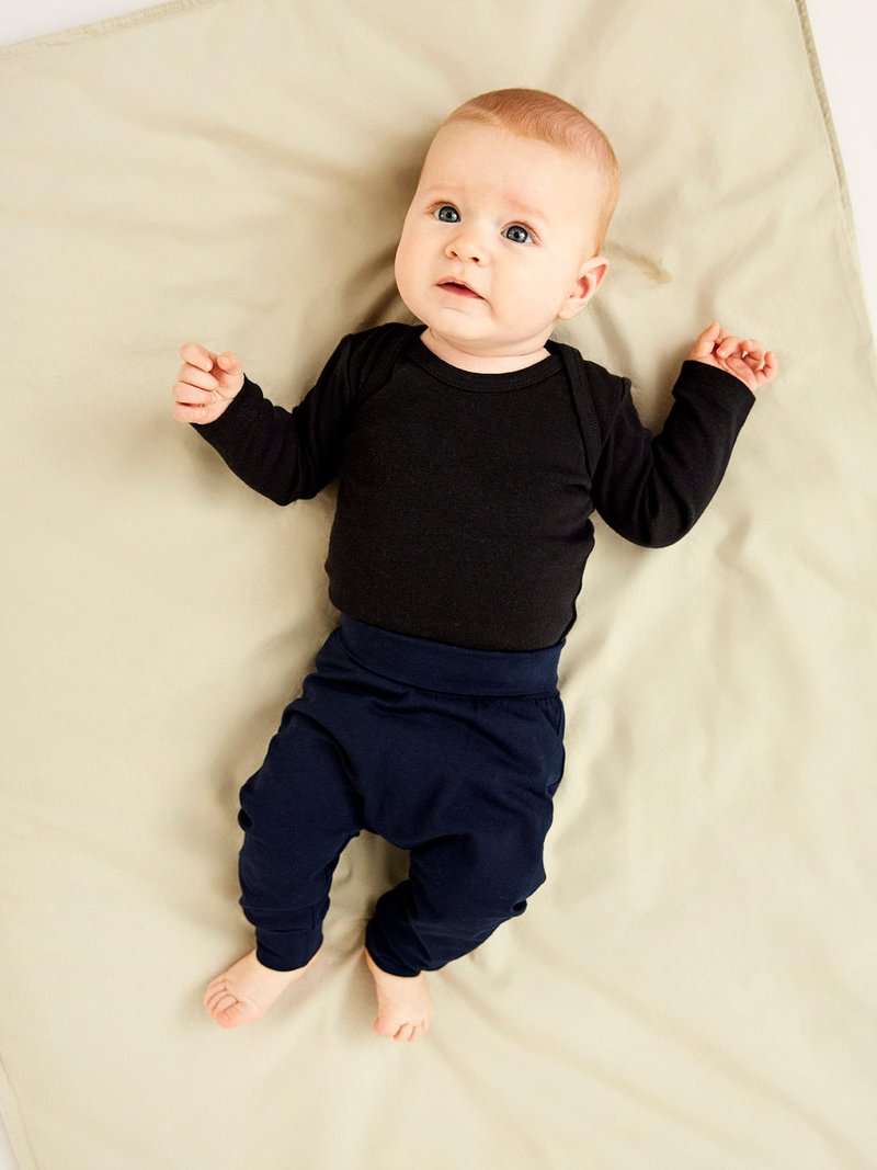 Svart långärmad bodysuit, marinblå byxor med manschetter, liggande på en ljusbeige yta. Bebis med ljust hår och blå ögon som tittar uppåt.