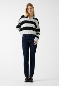 Pull court rayé noir et blanc avec un col à revers, assorti à un jean slim bleu foncé et des chaussures foncées. Texture lisse et côtelée.